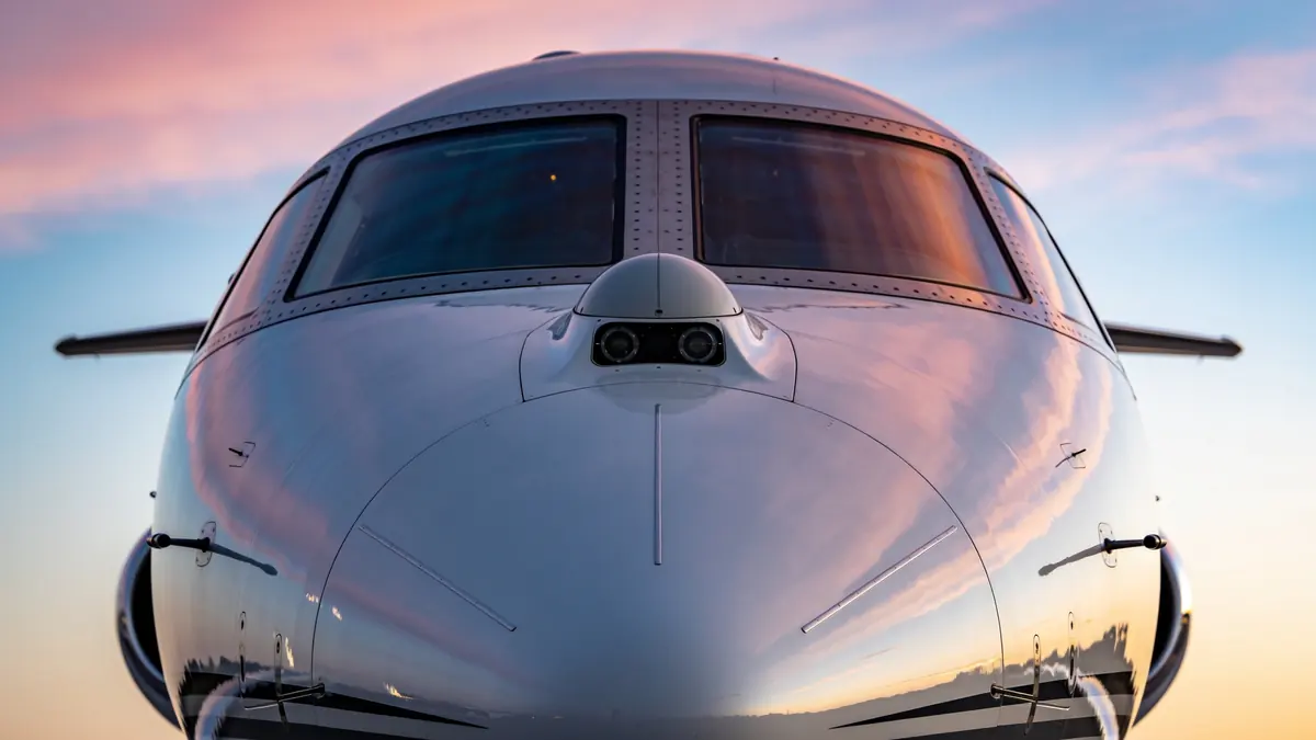 The clean nose and windscreen of a business jet reflecting a dawn sky.
